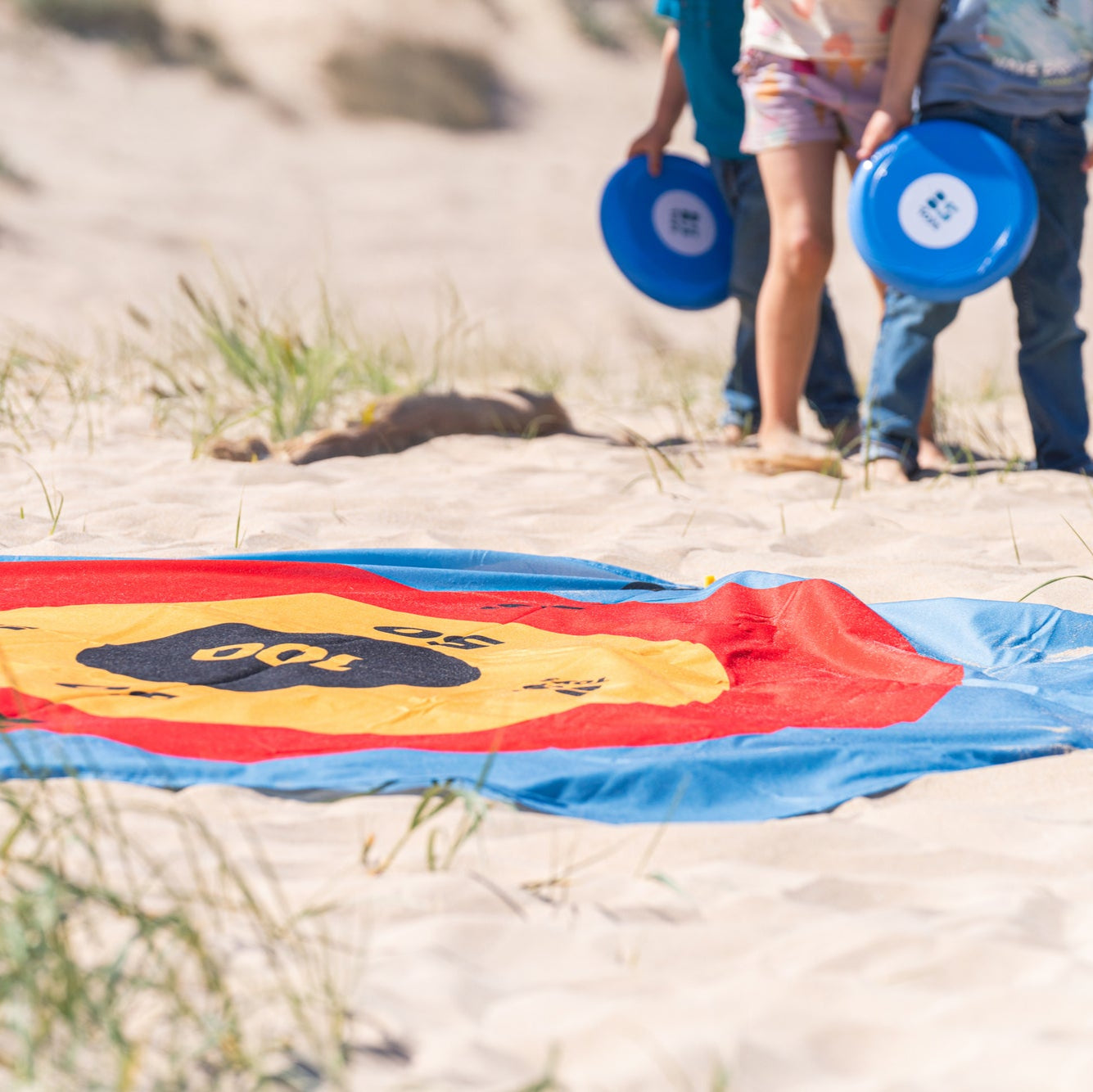 Scoring mat on sand with people holding frisbees in the background